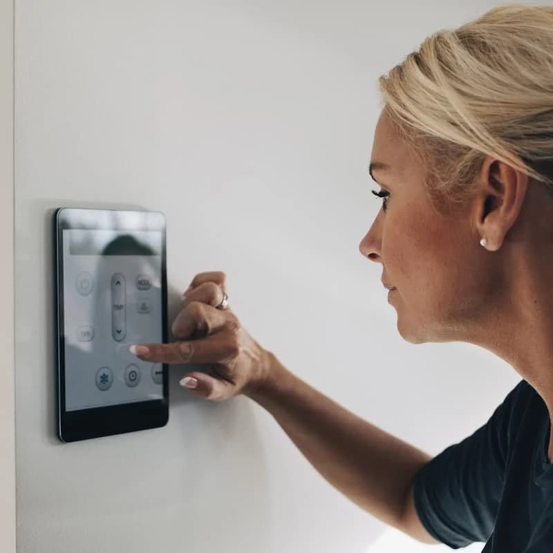 Woman using a thermostat app on a wall-mounted touch screen.