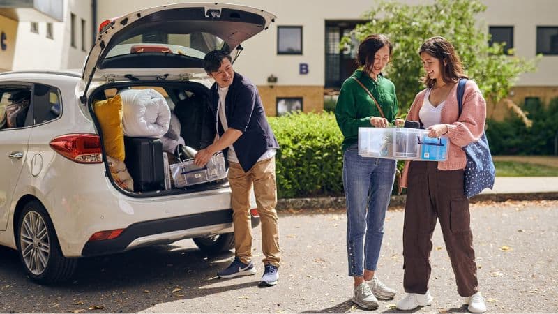man putting a box in the car and two women holding a box together