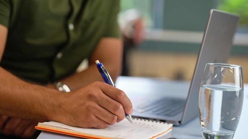 man leaning on desk writing in his notebook