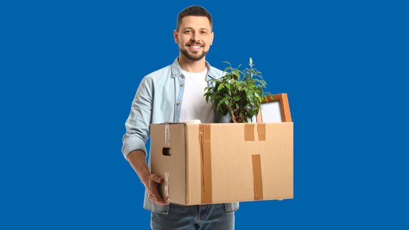 Man holding a packing box which contains a plant and picture frame