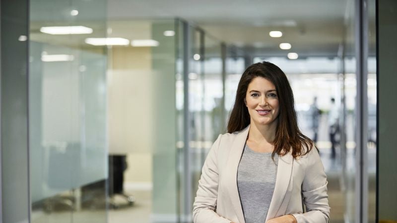 Woman in white blazer and grey shirt smiling while standing in an office